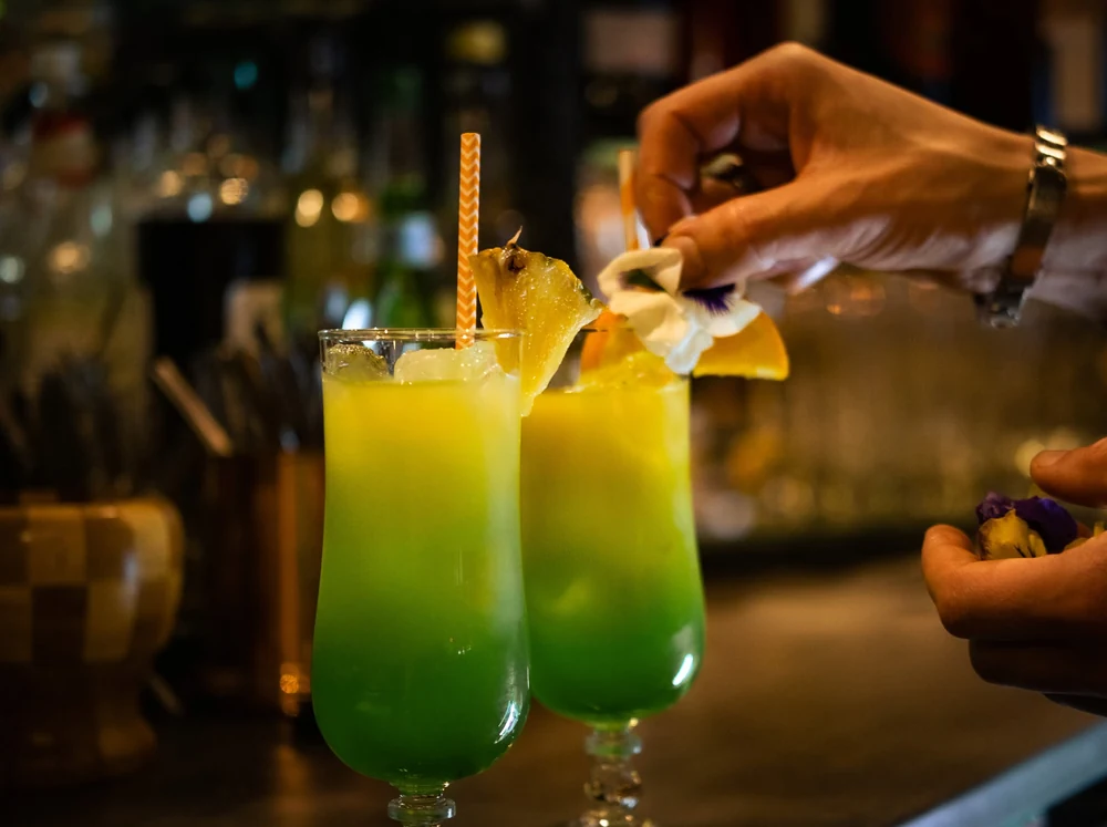 Préparation de deux cocktails jaunes et verts garnis de fruits.