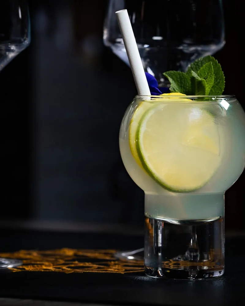 Cocktail clair dans un verre à pied, garni de citron vert et de menthe.