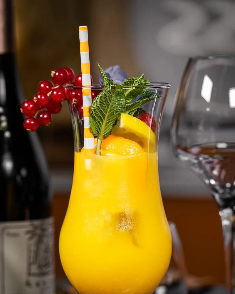 Cocktail jaune garni d’agrumes, de menthe et de groseilles rouges.
